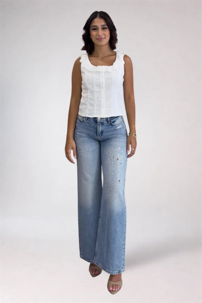 Woman wearing a white sleeveless top and blue jeans on a plain background