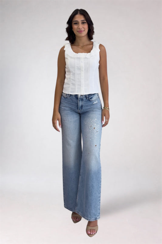 Woman wearing a white sleeveless top and blue jeans on a plain background