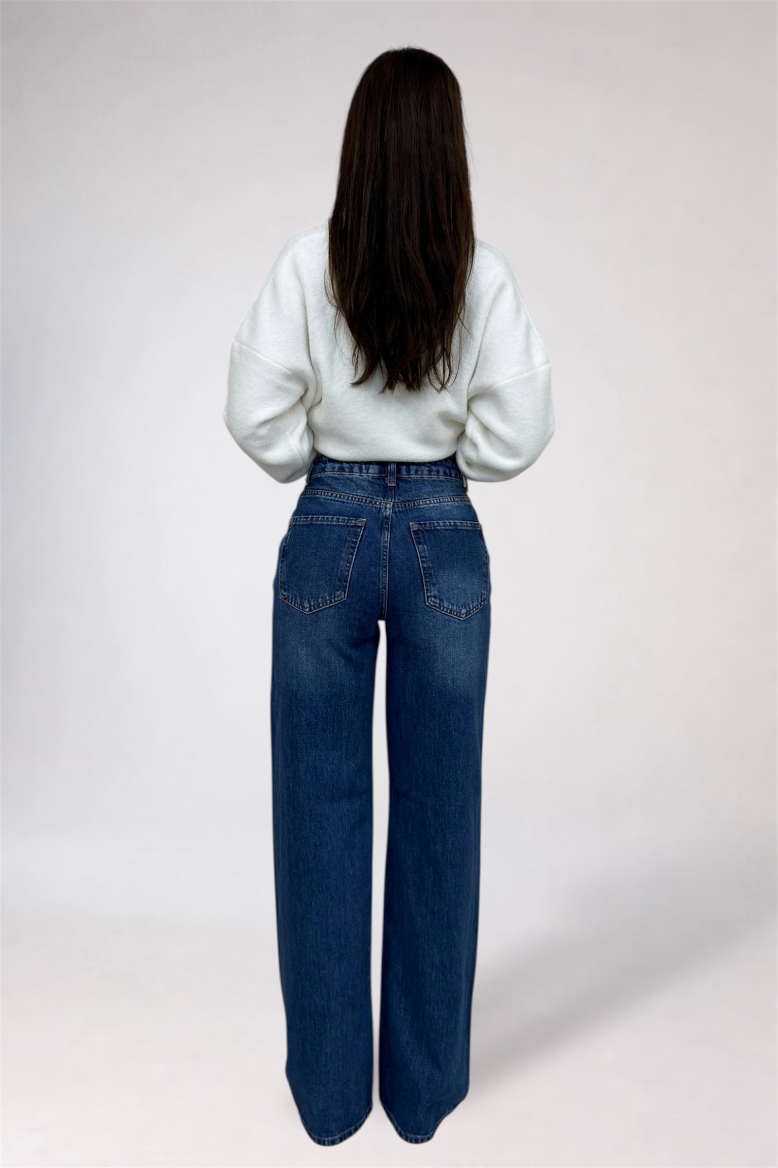 Person wearing blue jeans and a white top on a plain background