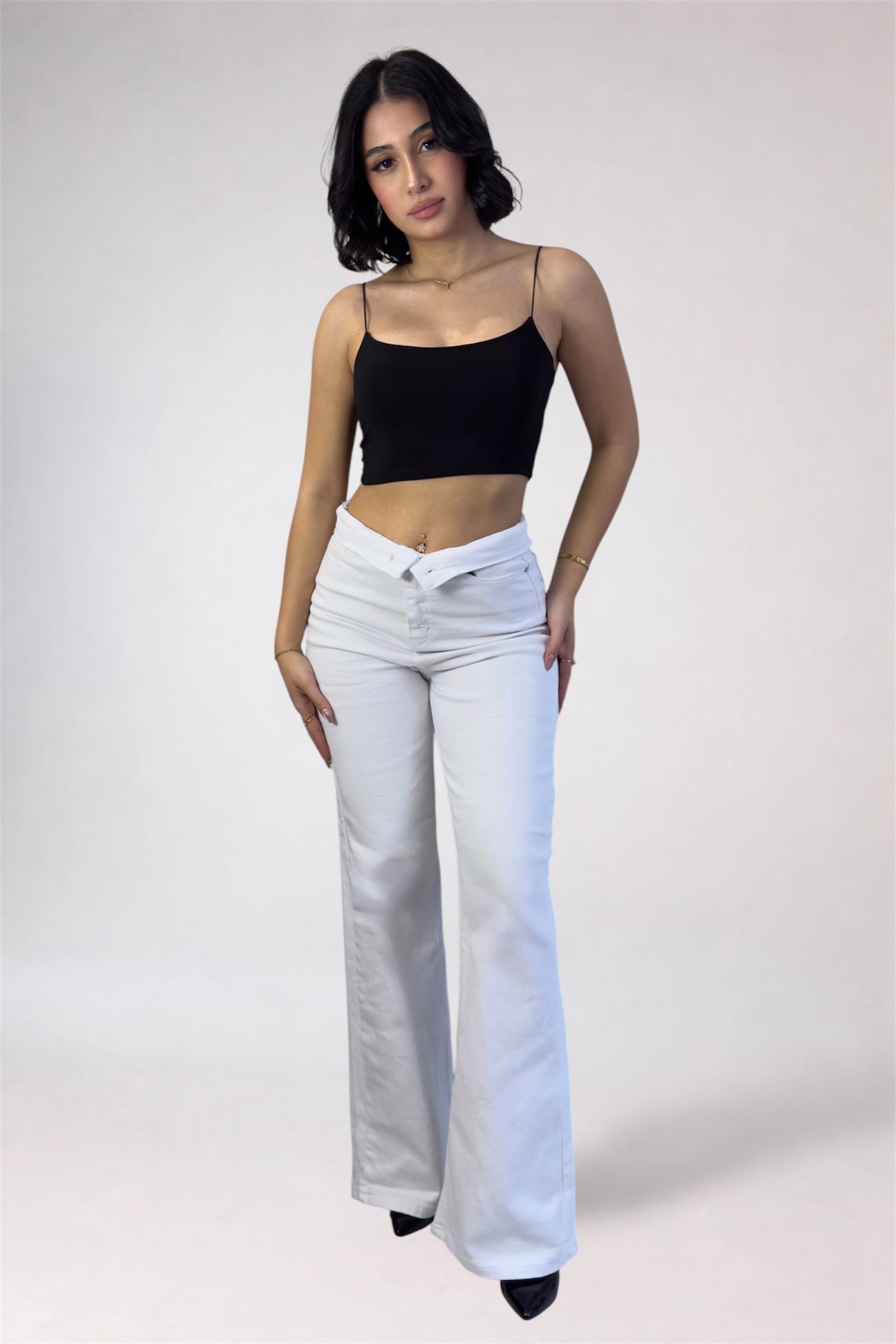 Woman wearing a black top and white pants on a plain background