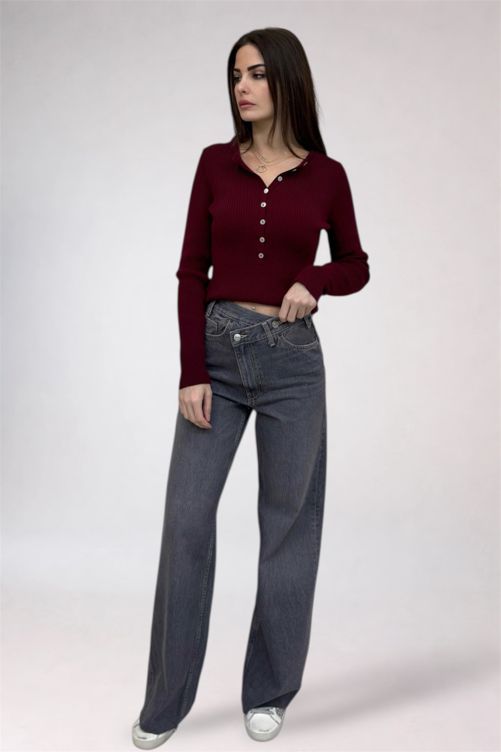 Woman wearing a burgundy long-sleeve top and gray jeans on a white background