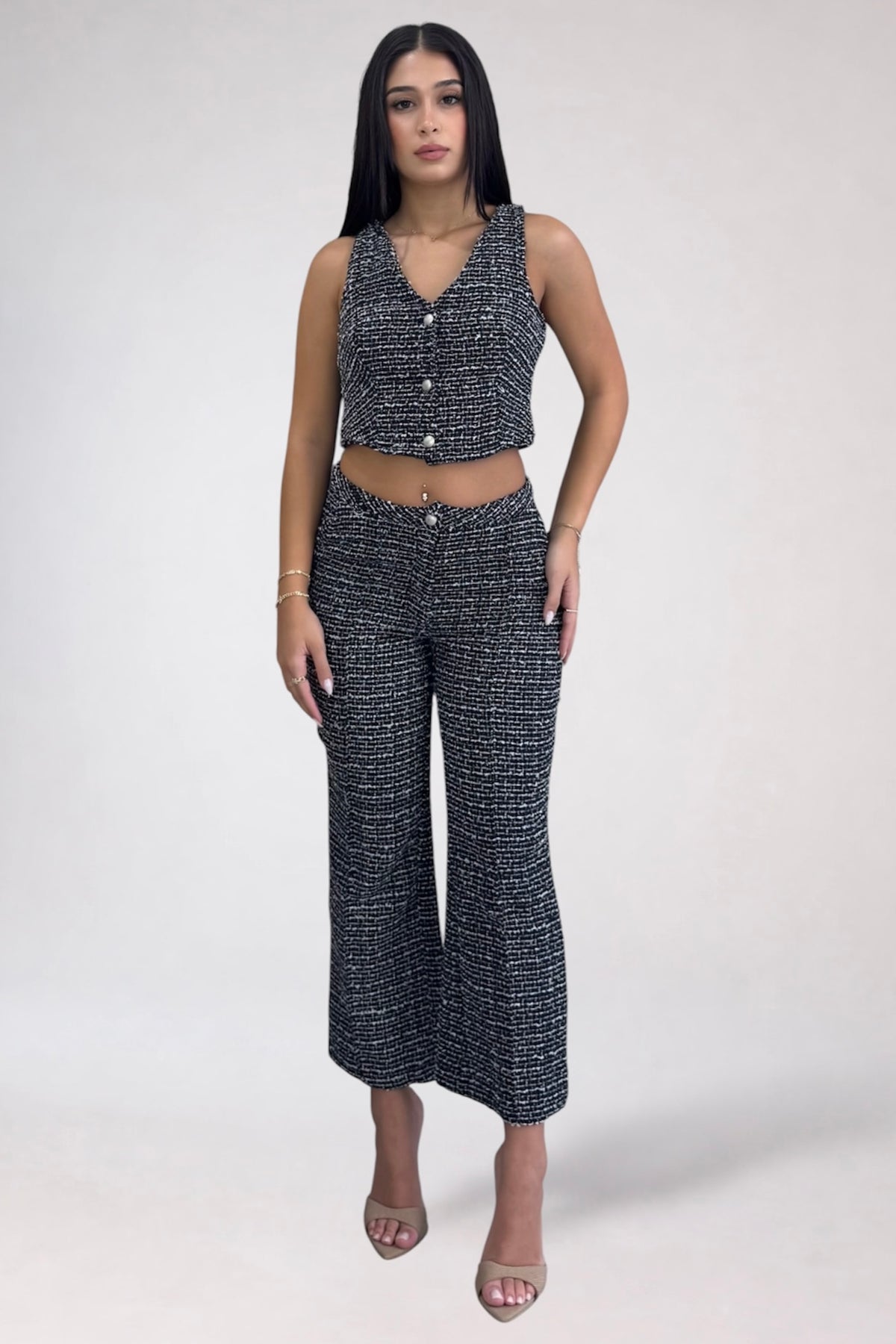 A woman modeling a matching sleeveless cropped top and wide-leg pants set in a black and white textured tweed fabric, photographed against a plain light gray studio background.