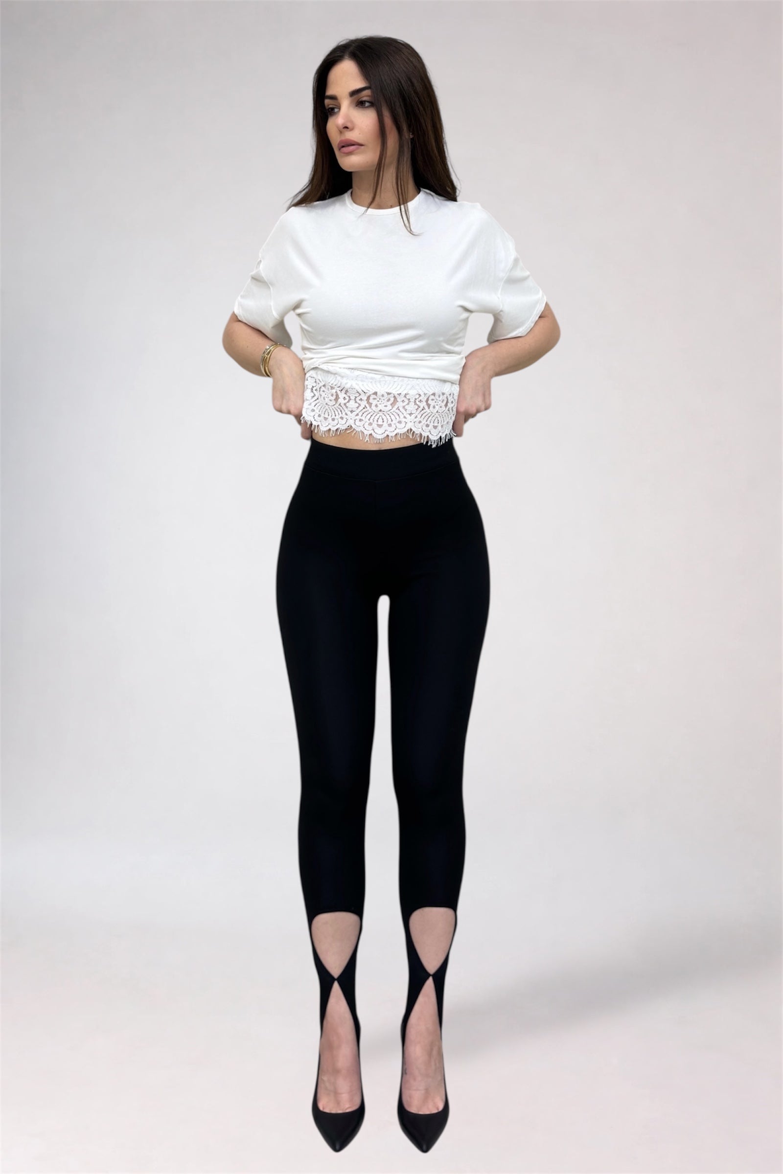 Woman wearing a white cropped top and black leggings with cut-out design on a plain background