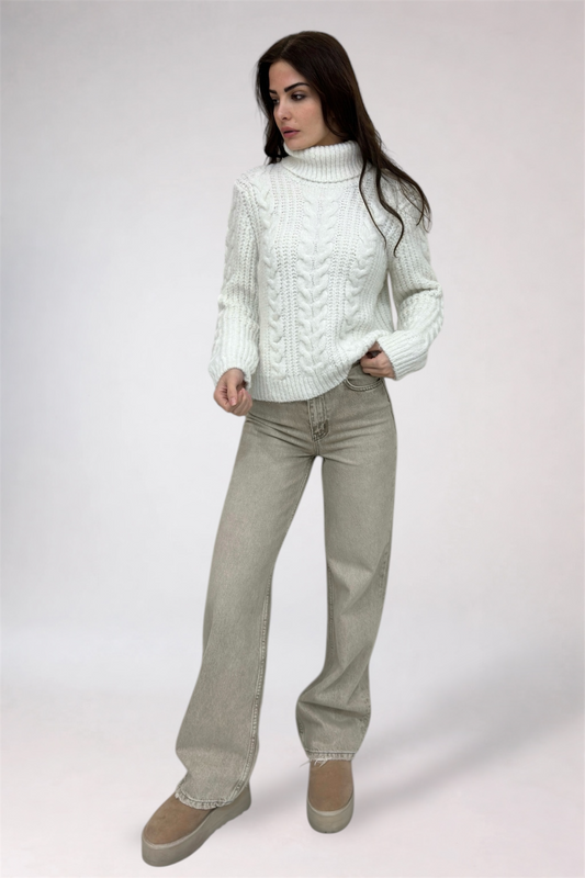 Woman wearing a white cable knit sweater and beige pants on a white background