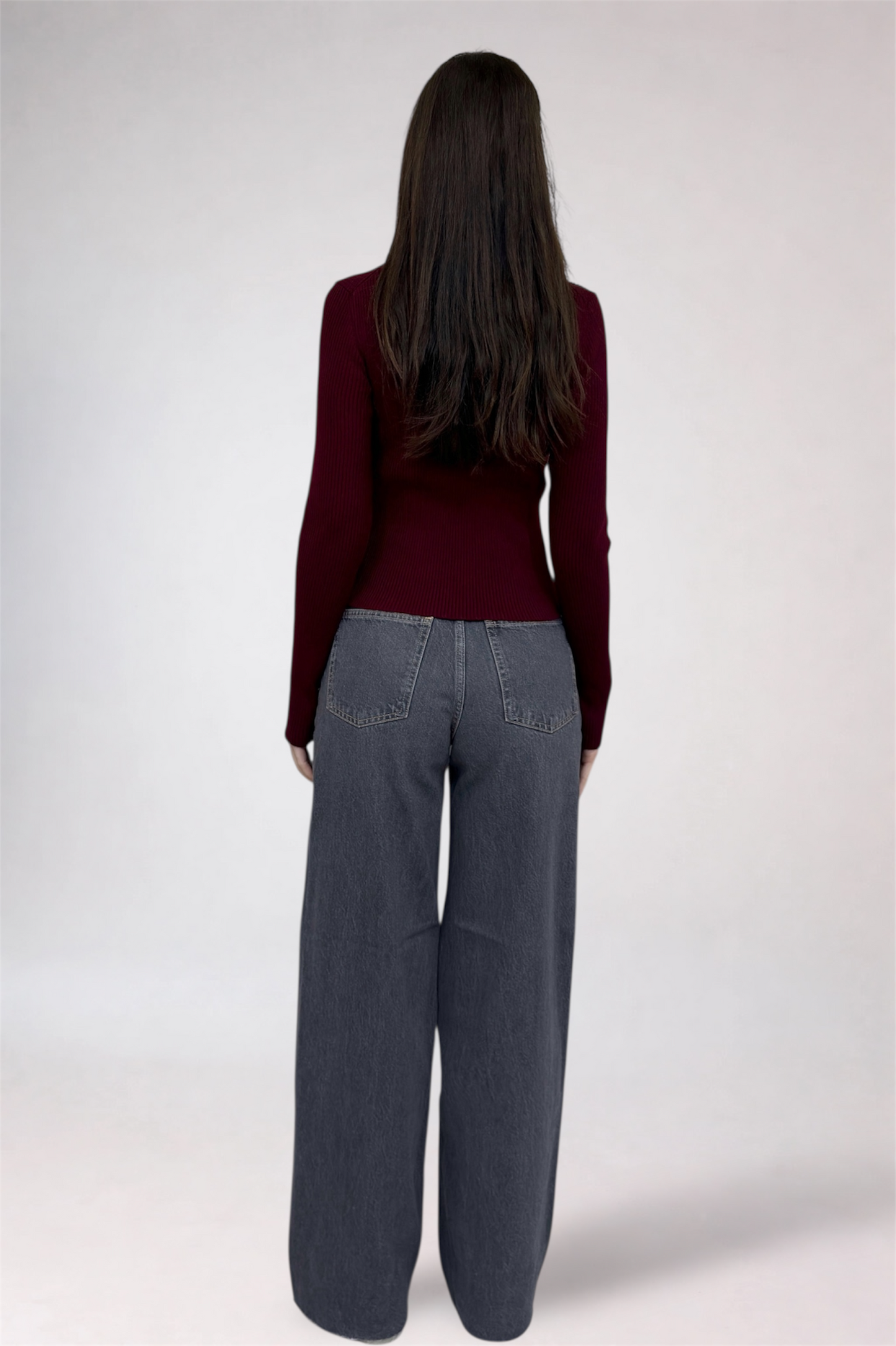 Person wearing a burgundy sweater and gray pants on a white background