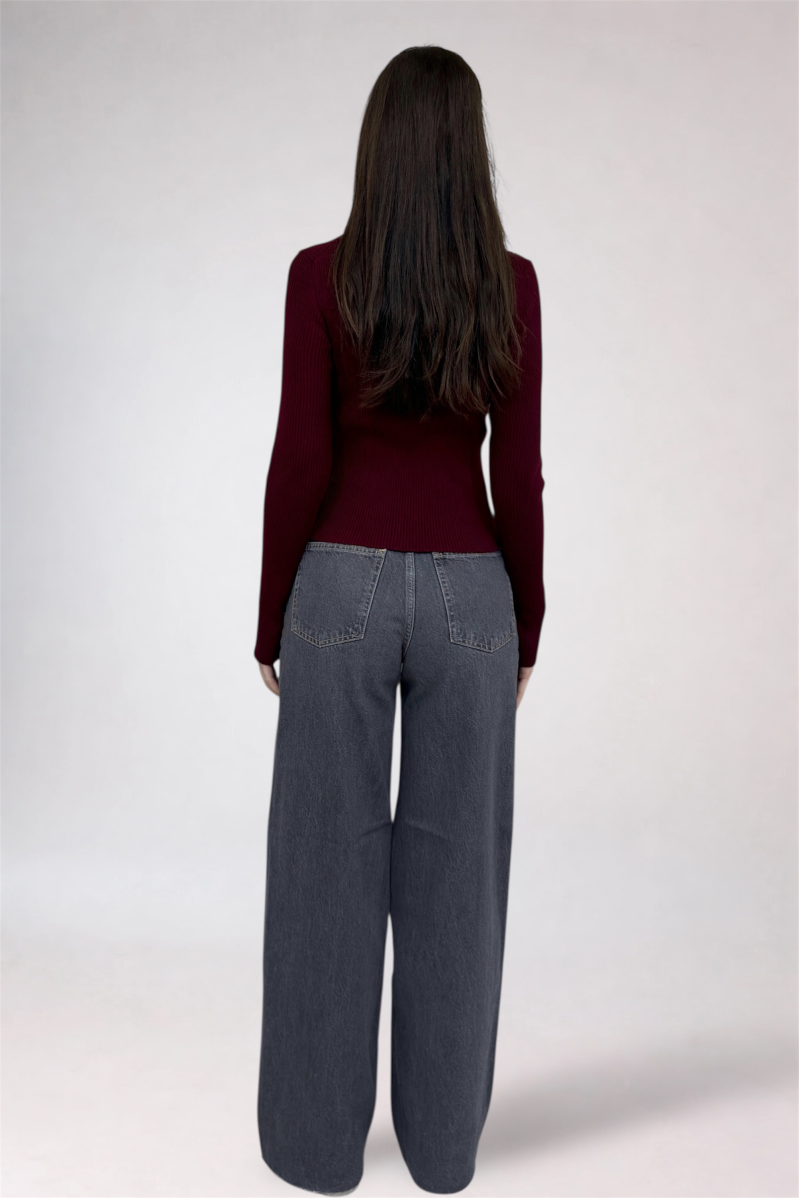 Person wearing a burgundy sweater and gray pants on a white background