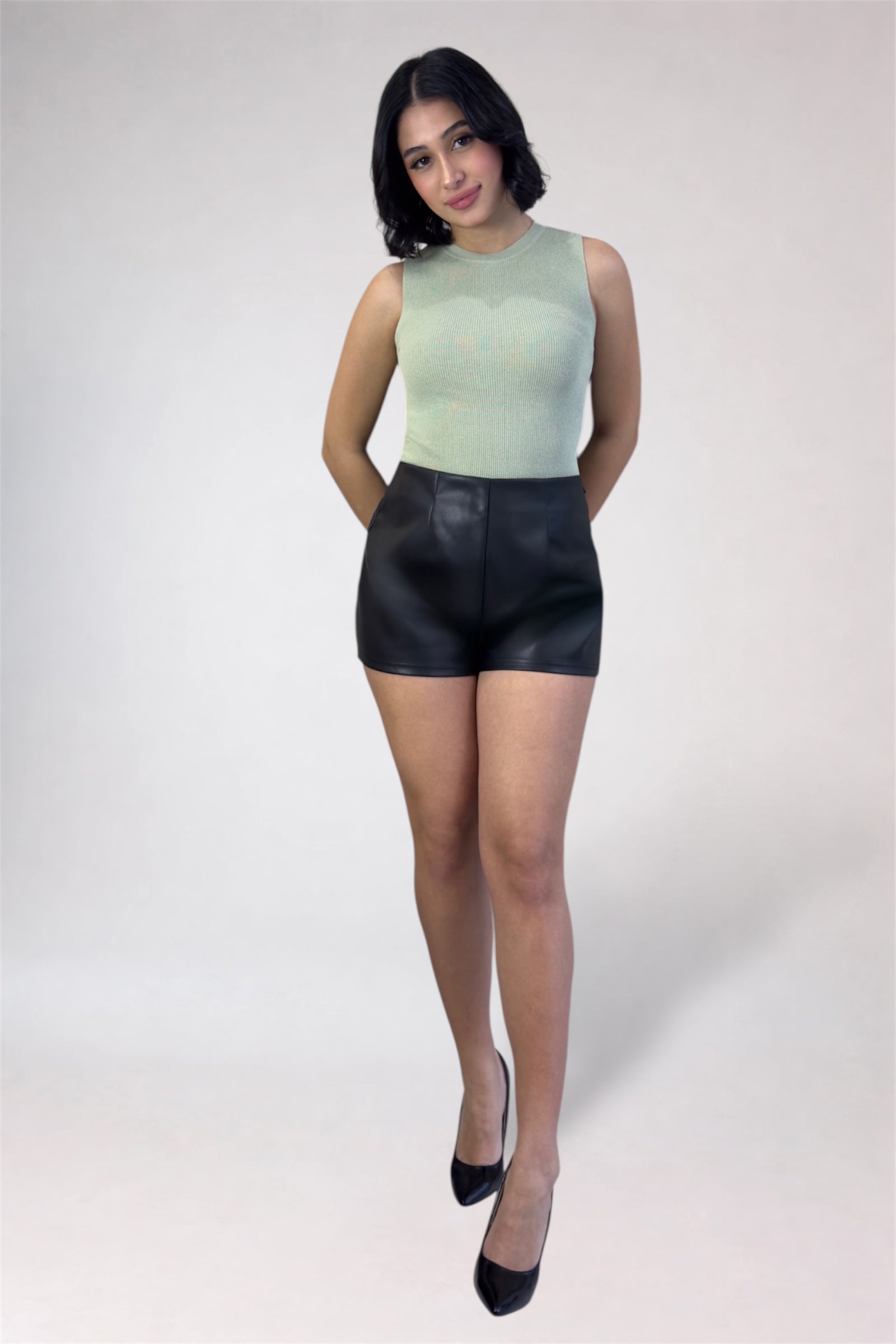Woman wearing a light green sleeveless top and black leather shorts on a white background