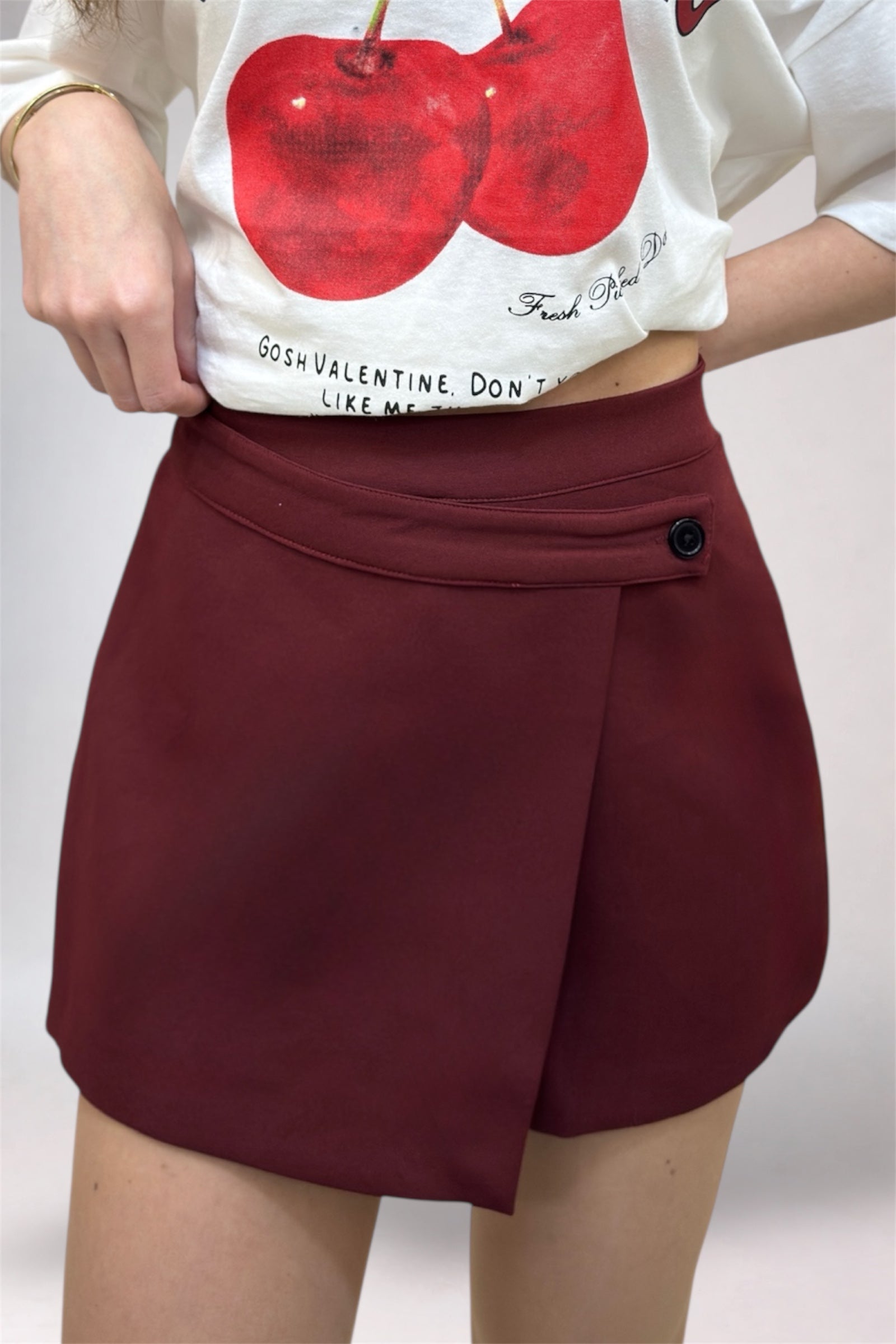 Person wearing a white t-shirt with red graphics and maroon shorts on a plain background