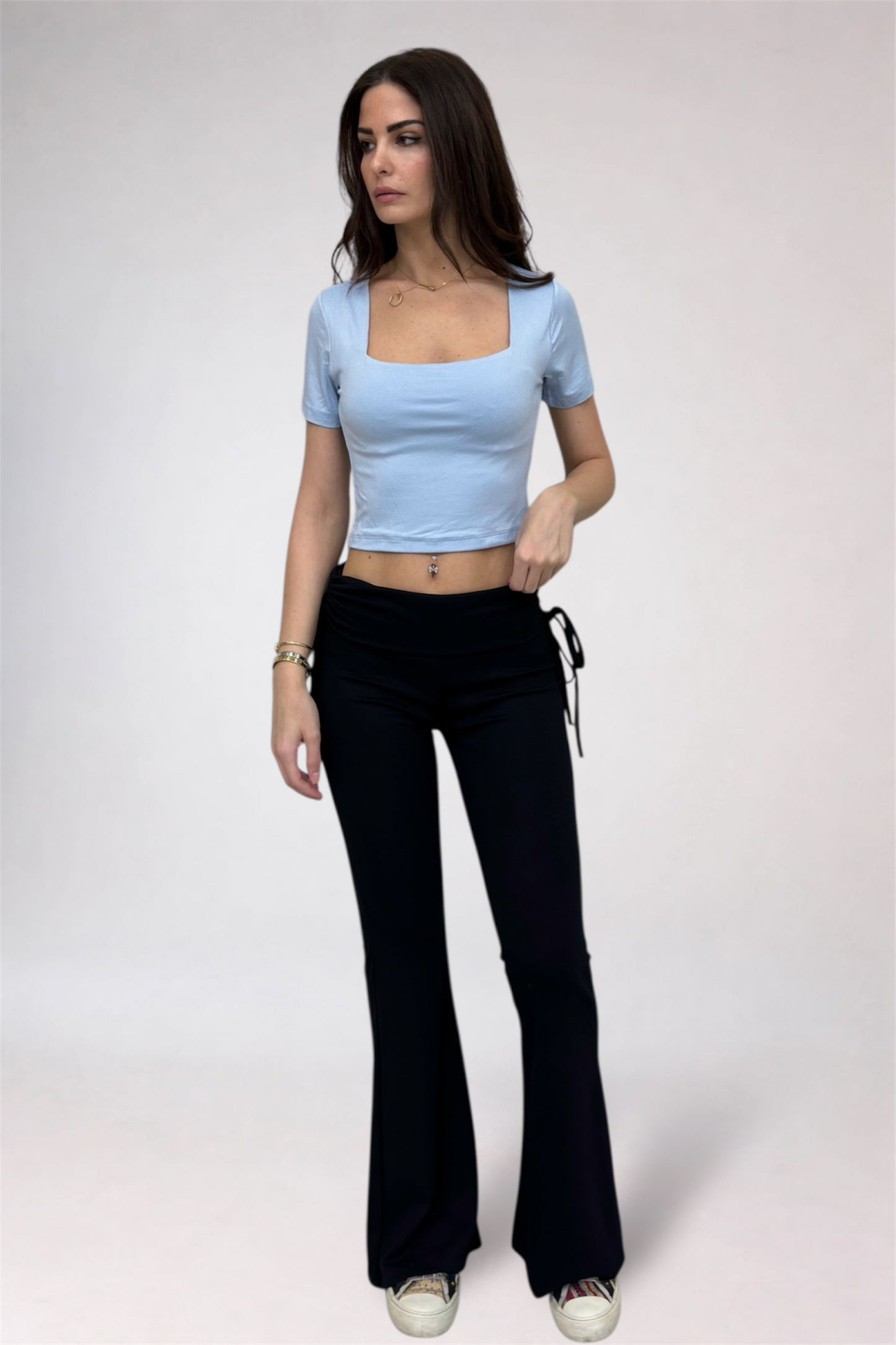 Woman wearing a light blue top and black flared pants on a white background