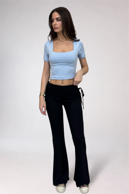 Woman wearing a light blue top and black flared pants on a white background