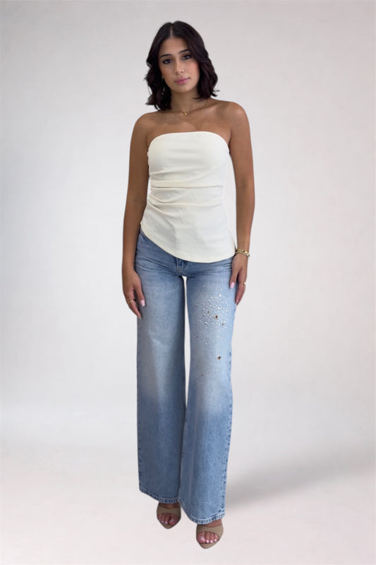 Woman wearing a white strapless top and blue jeans on a plain background