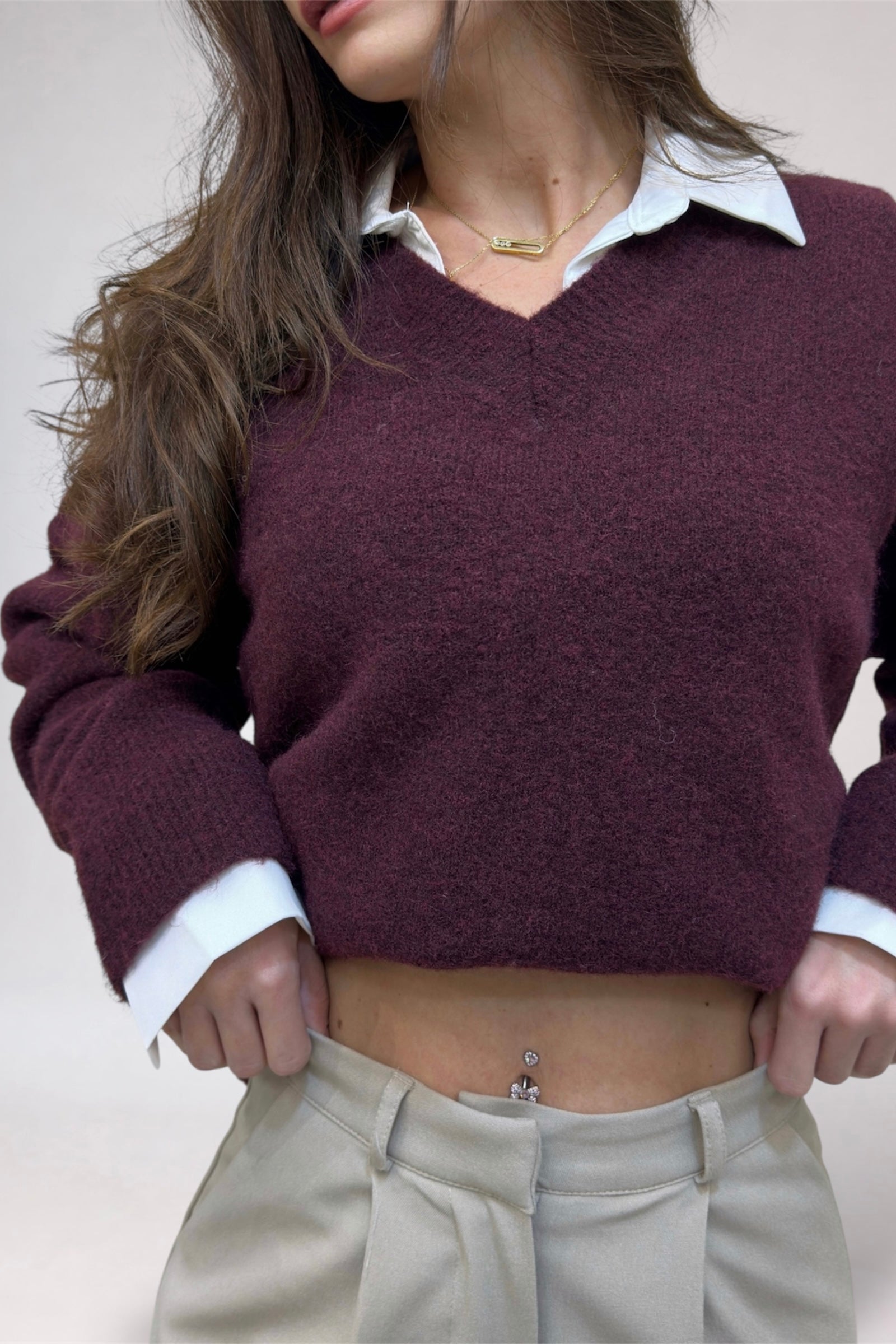 Person wearing a maroon sweater over a white shirt with beige pants on a neutral background