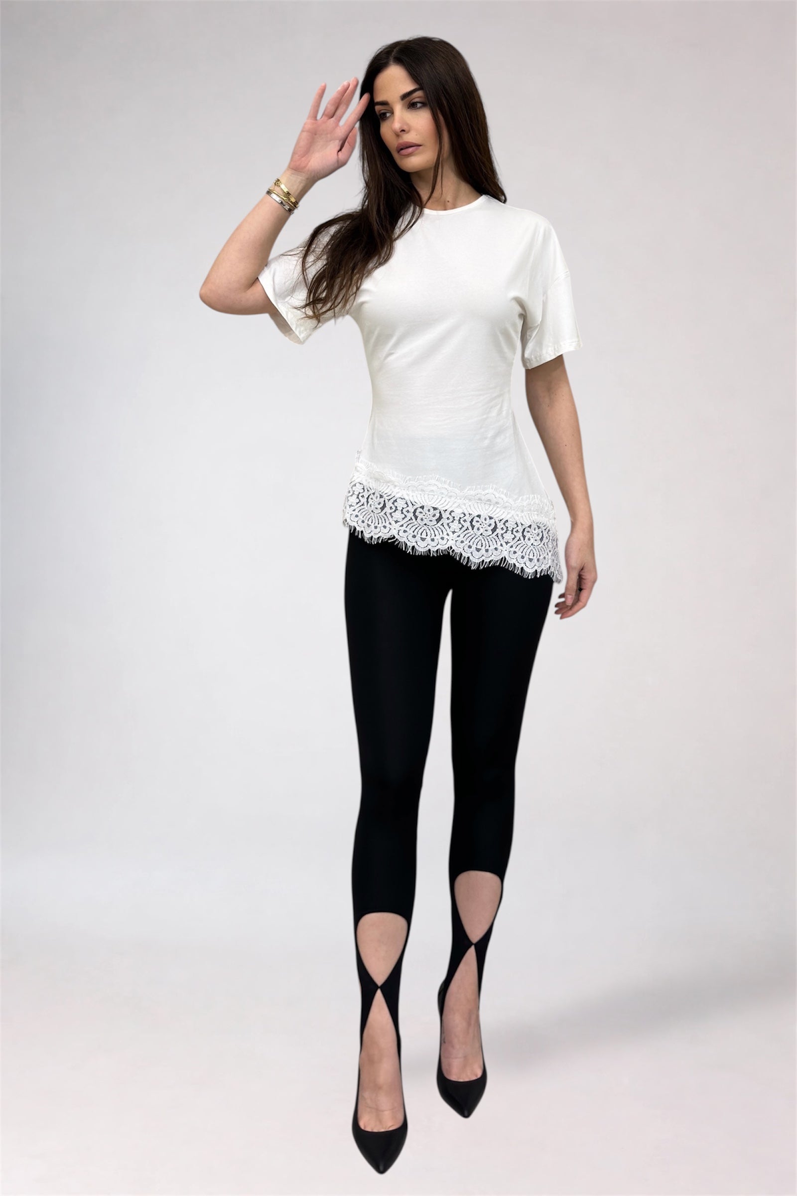 Woman wearing a white top with lace details and black leggings on a white background