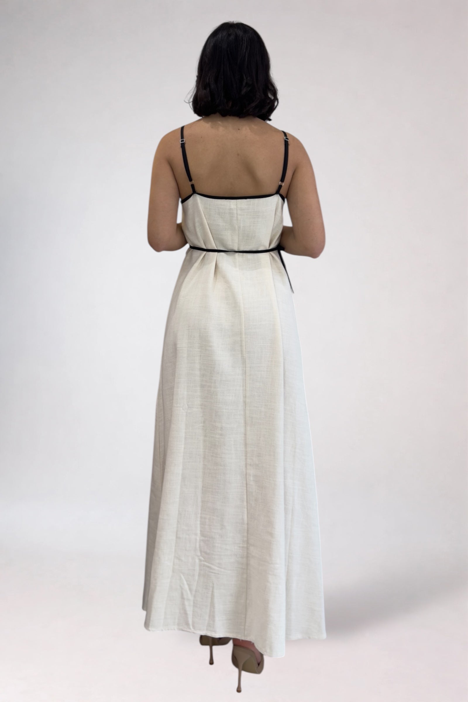 Woman wearing a white dress with black straps on a plain background