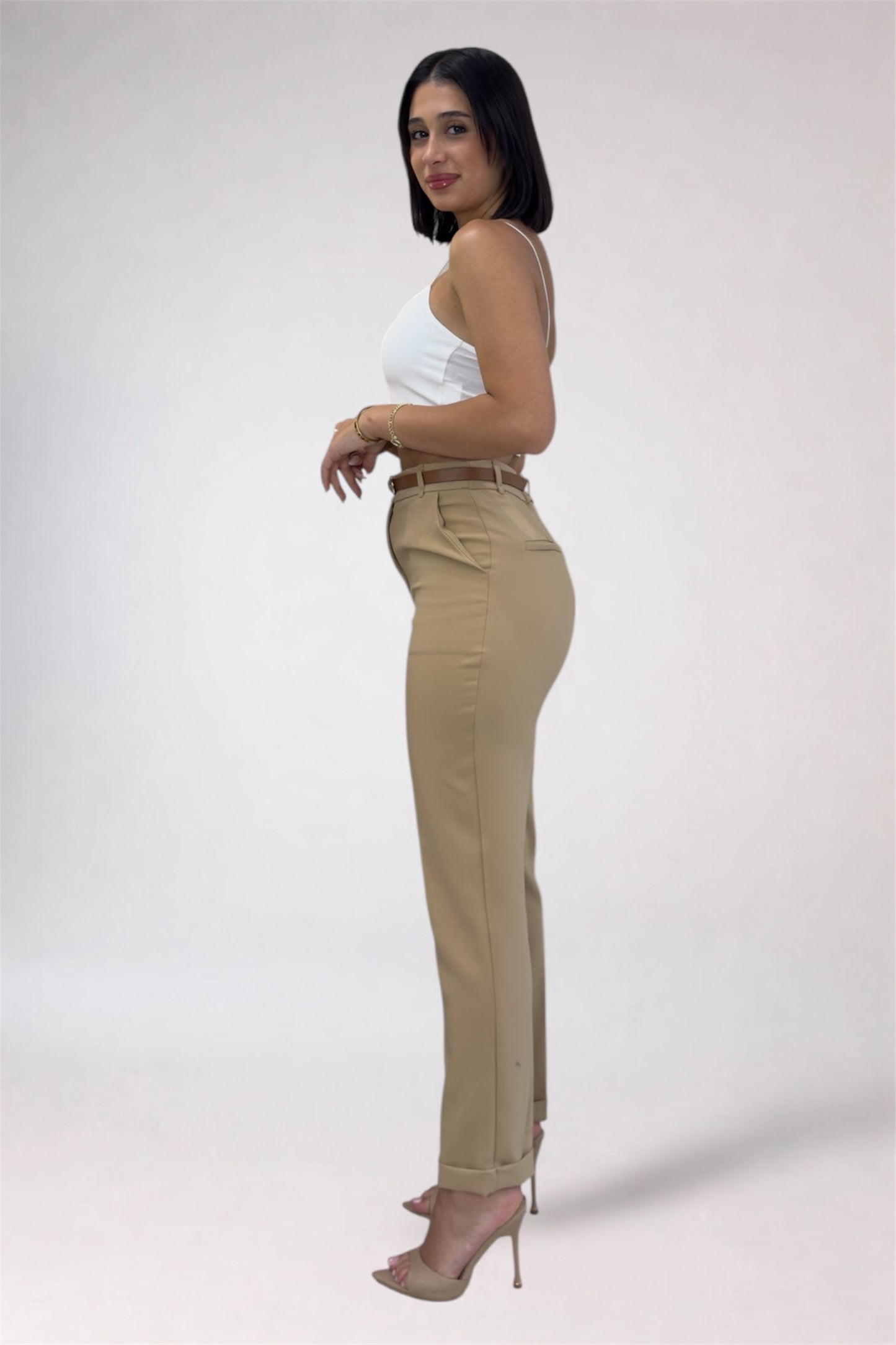 Woman wearing beige pants and a white top on a plain background