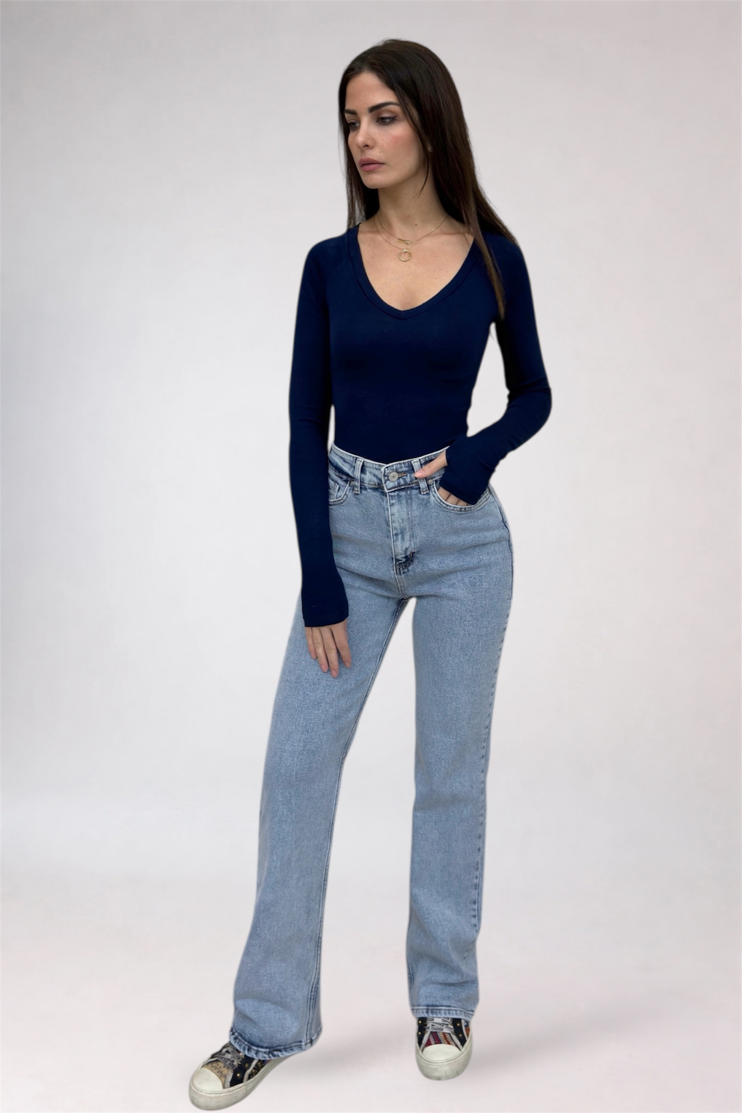 Woman wearing a navy long-sleeve top and light blue jeans on a white background