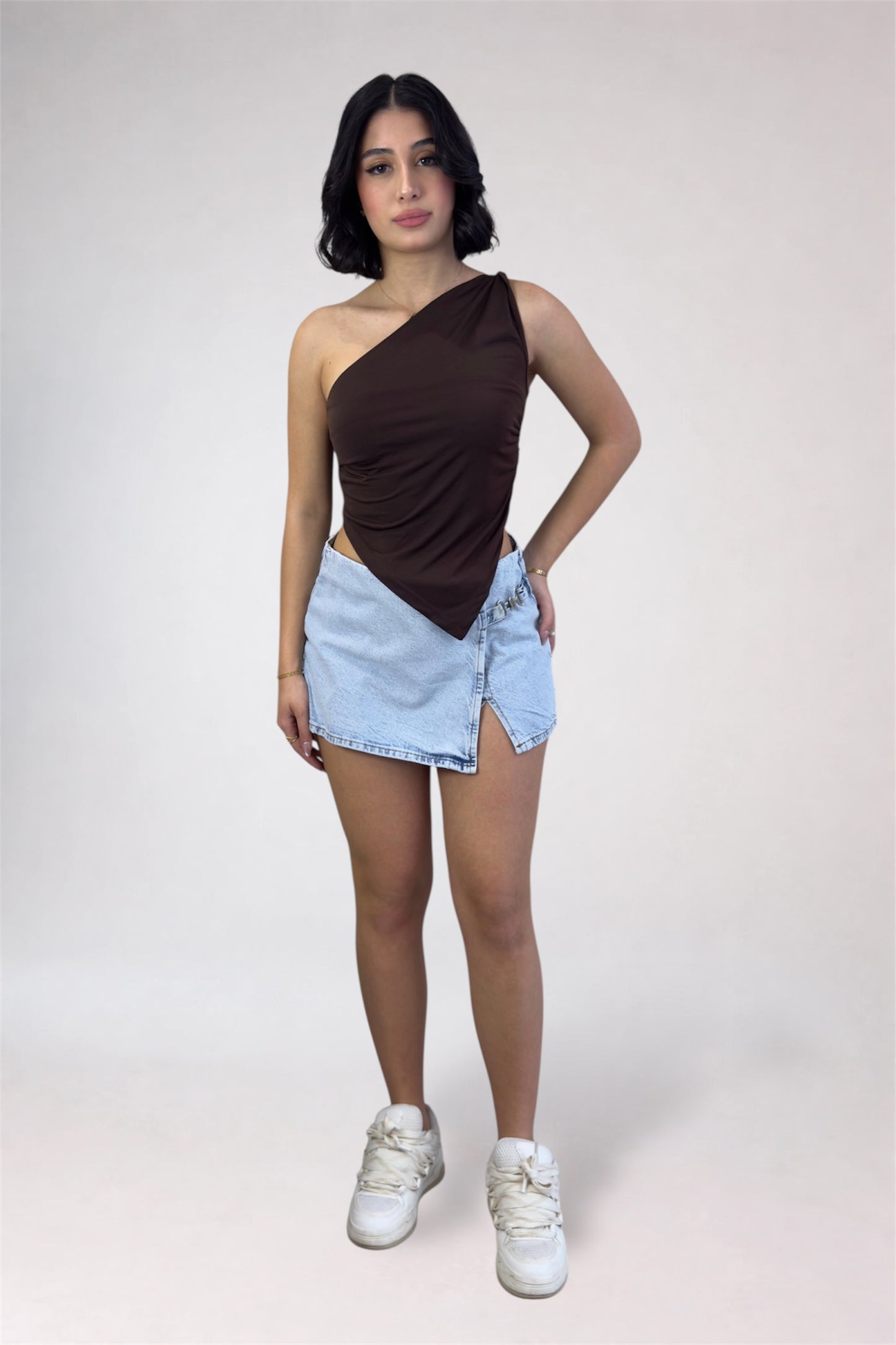 Woman wearing a brown one-shoulder top and light blue denim shorts on a white background