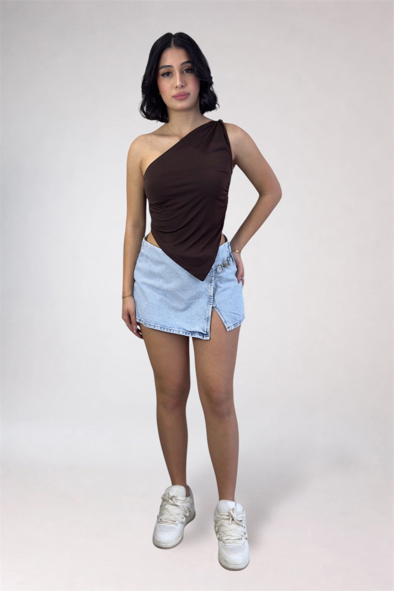 Woman wearing a brown one-shoulder top and light blue denim shorts on a white background