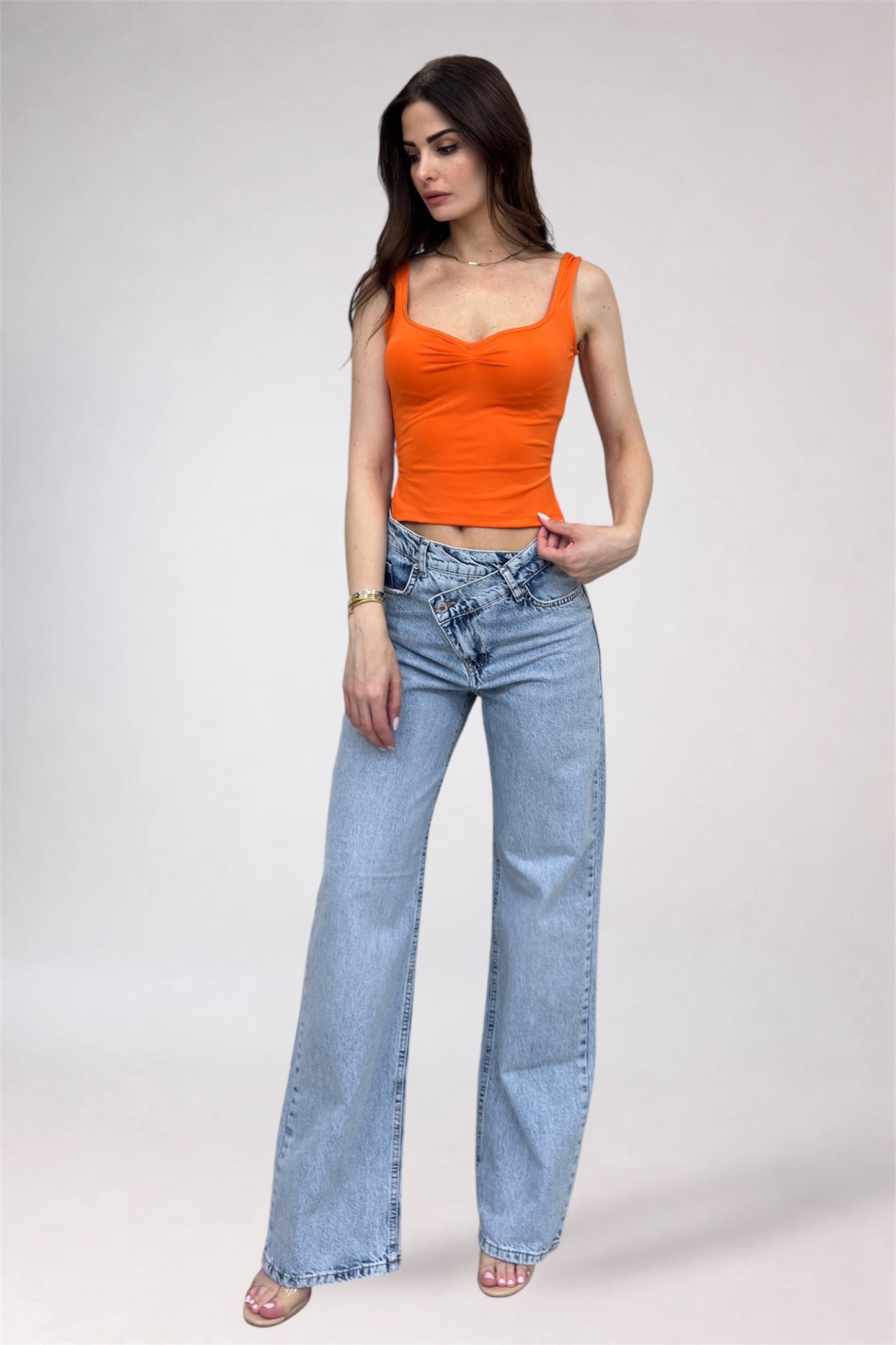 Woman wearing an orange top and blue jeans on a plain background