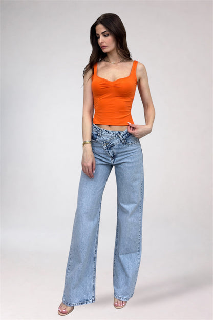 Woman wearing an orange top and blue jeans on a plain background