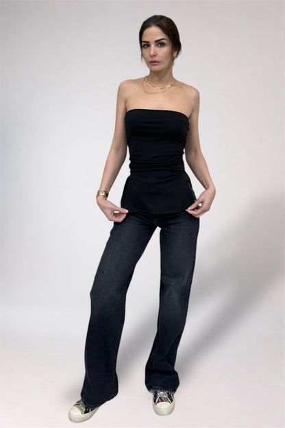 Woman wearing a black strapless top and dark jeans on a white background