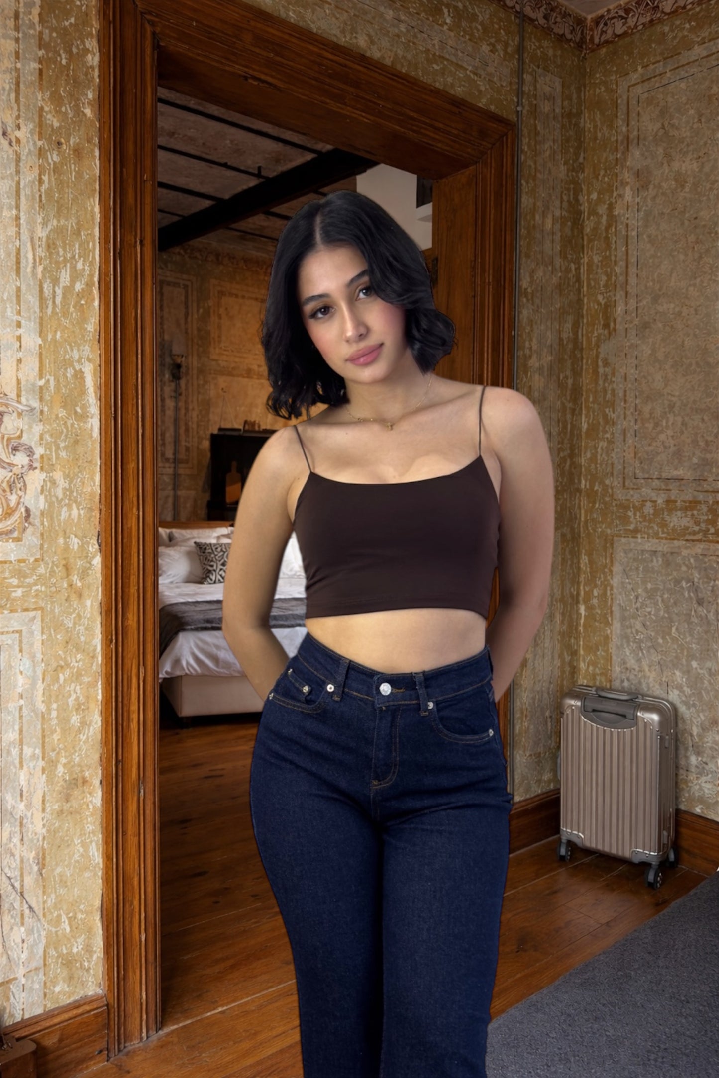 Woman standing in a room with stone walls and wooden floor, wearing a brown top and blue jeans.