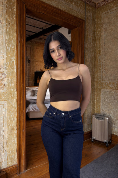 Woman standing in a room with stone walls and wooden floor, wearing a brown top and blue jeans.