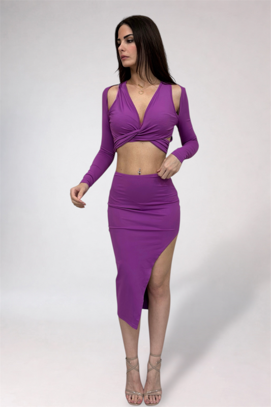 Woman wearing a purple outfit with long sleeves and a high slit skirt on a white background