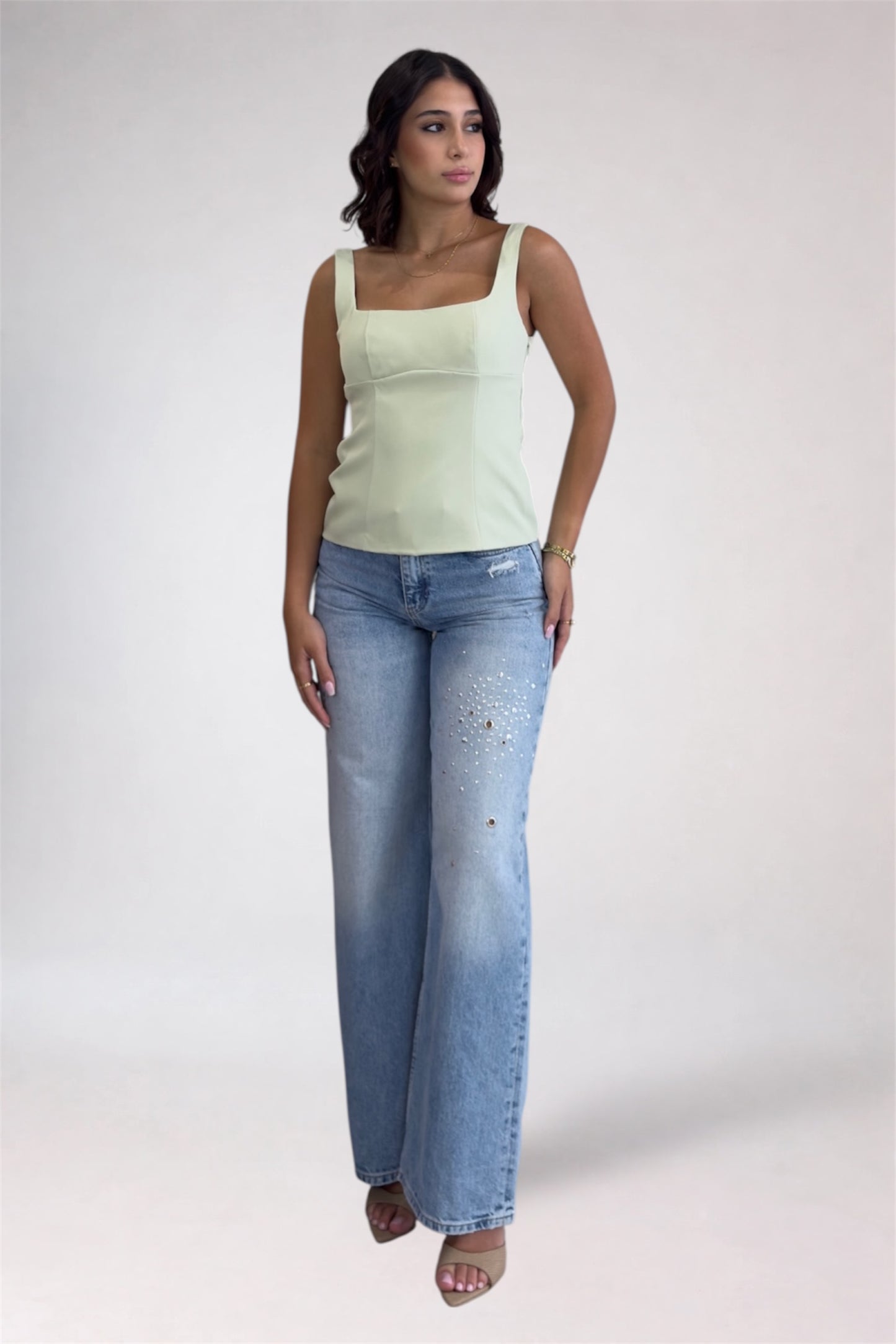Woman wearing a light green tank top and blue jeans on a white background