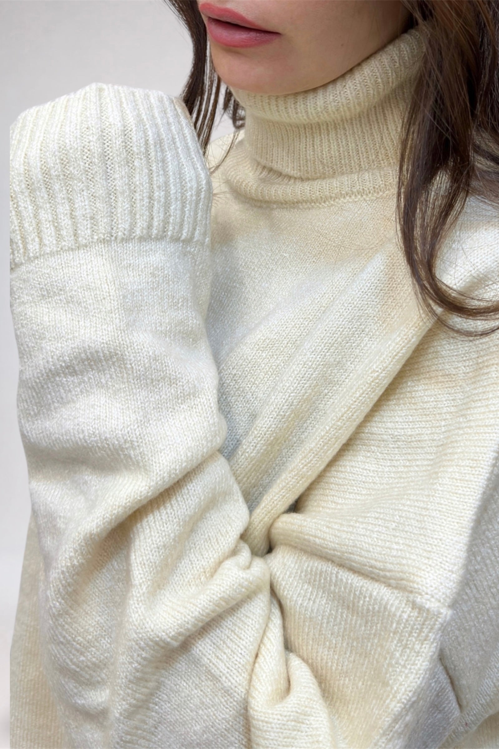 Close-up of a person wearing a cream-colored turtleneck sweater with a white coat.