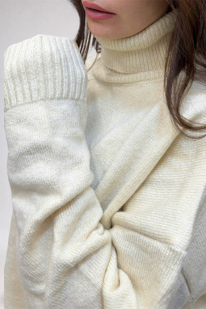 Close-up of a person wearing a cream-colored turtleneck sweater with a white coat.