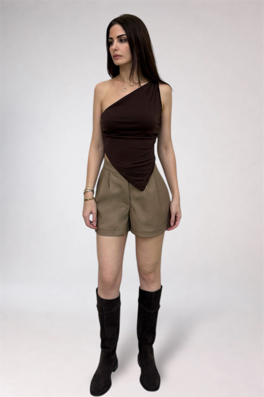 Woman wearing a brown one-shoulder top and beige shorts with black knee-high boots on a white background