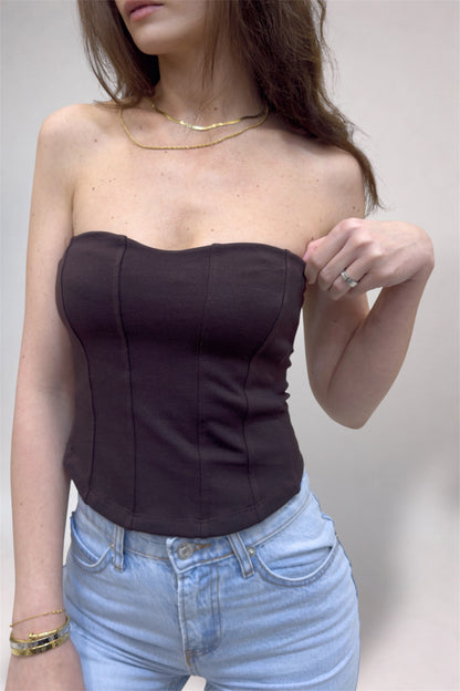 Woman wearing a black strapless top and light blue jeans against a neutral background