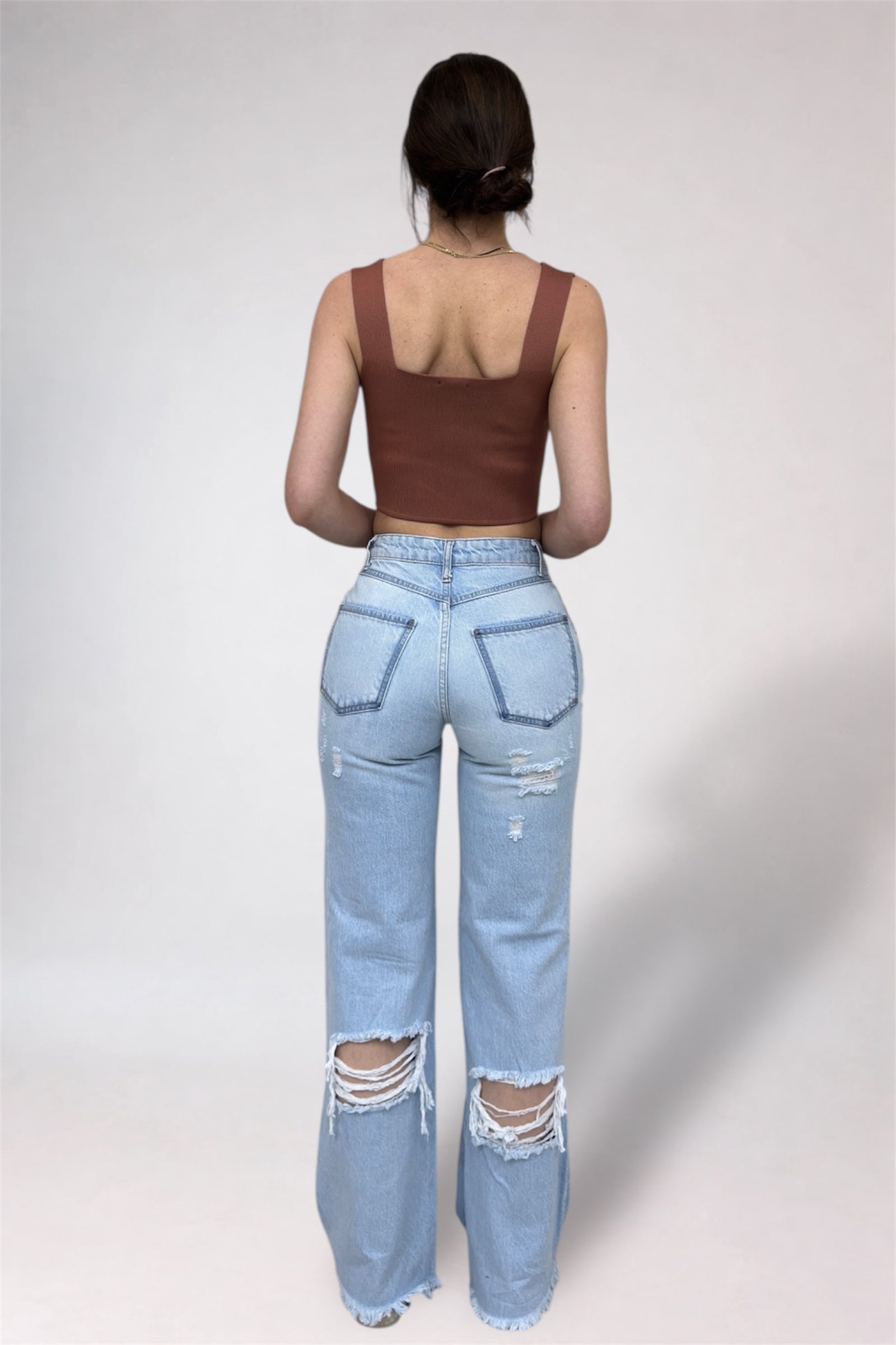 Person wearing a brown tank top and light blue ripped jeans on a white background