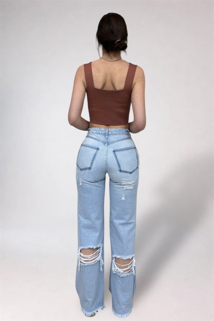Person wearing a brown tank top and light blue ripped jeans on a white background