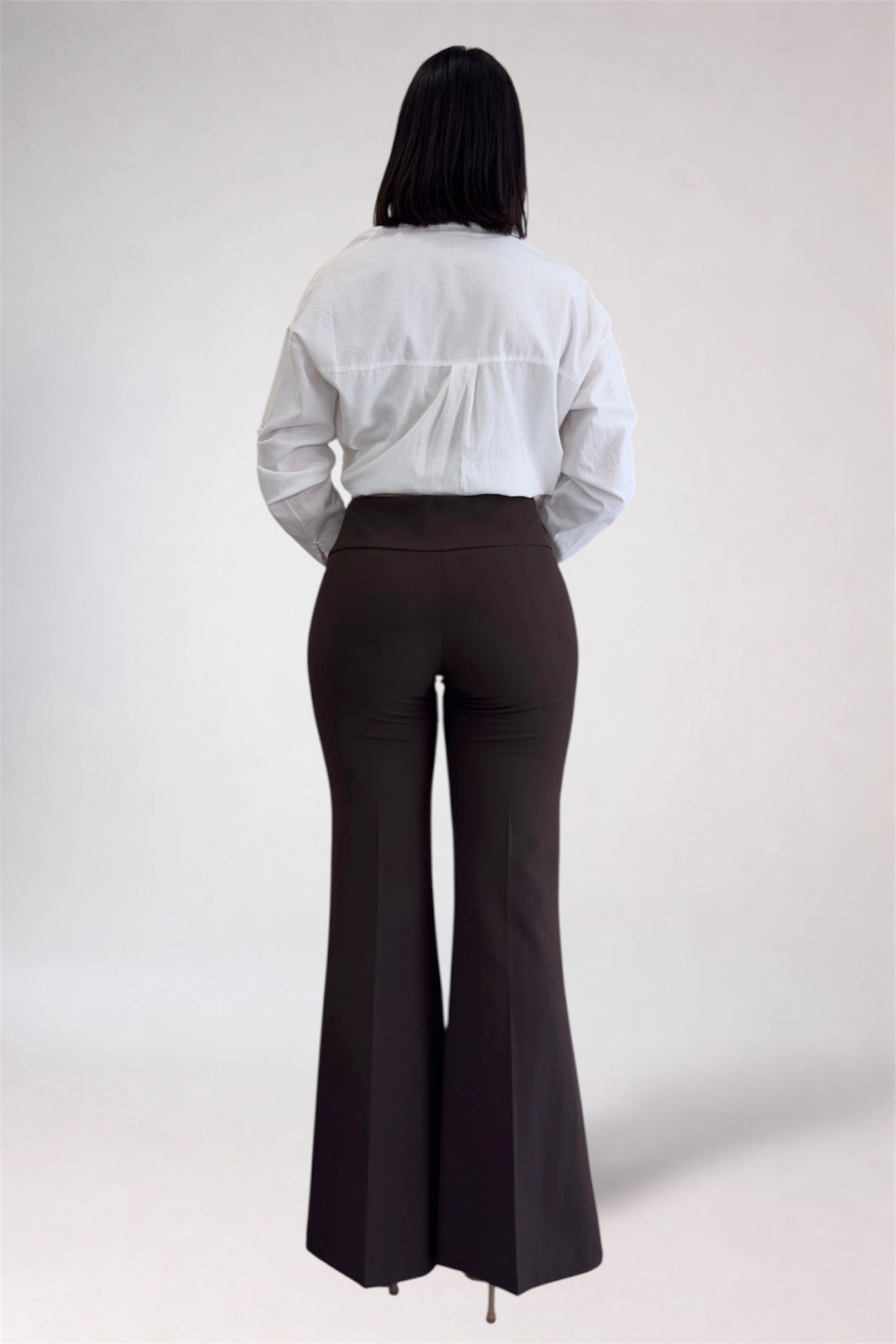 Person wearing a white shirt and brown flared pants on a plain background