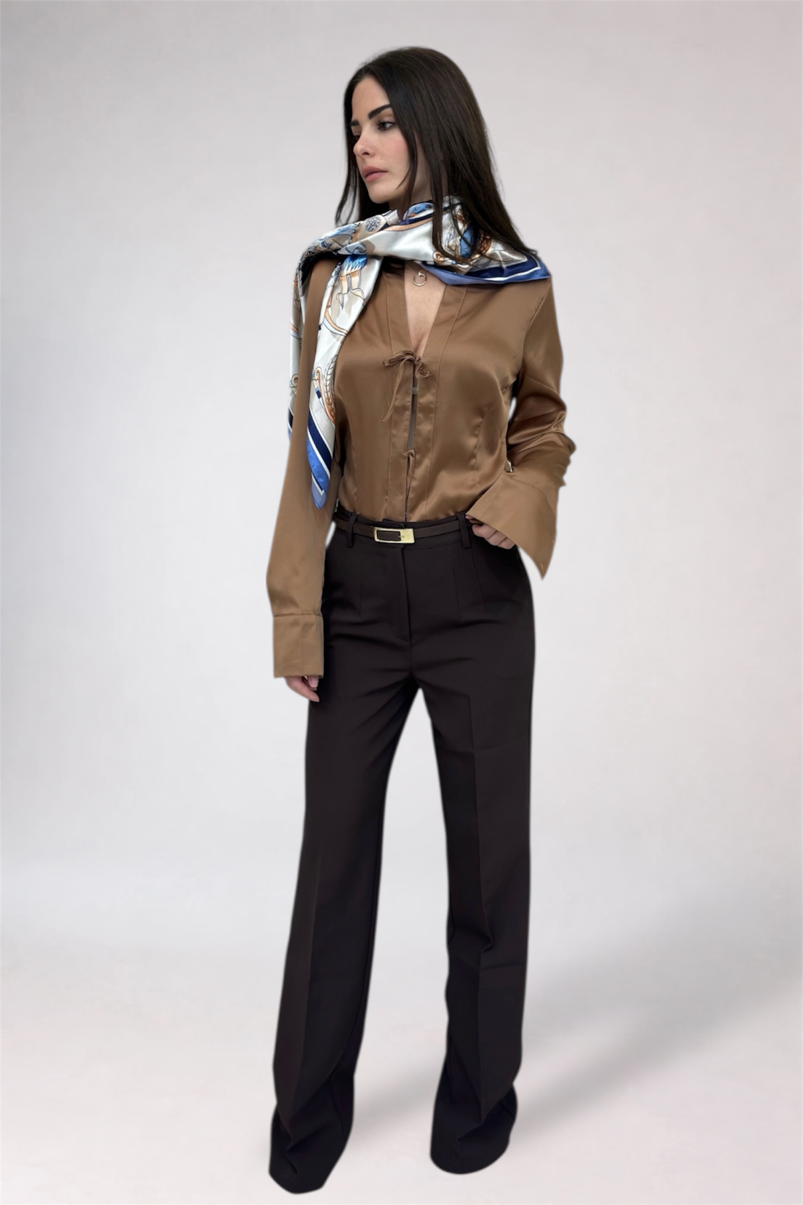 Woman wearing a brown satin shirt and black pants with a patterned scarf on a white background