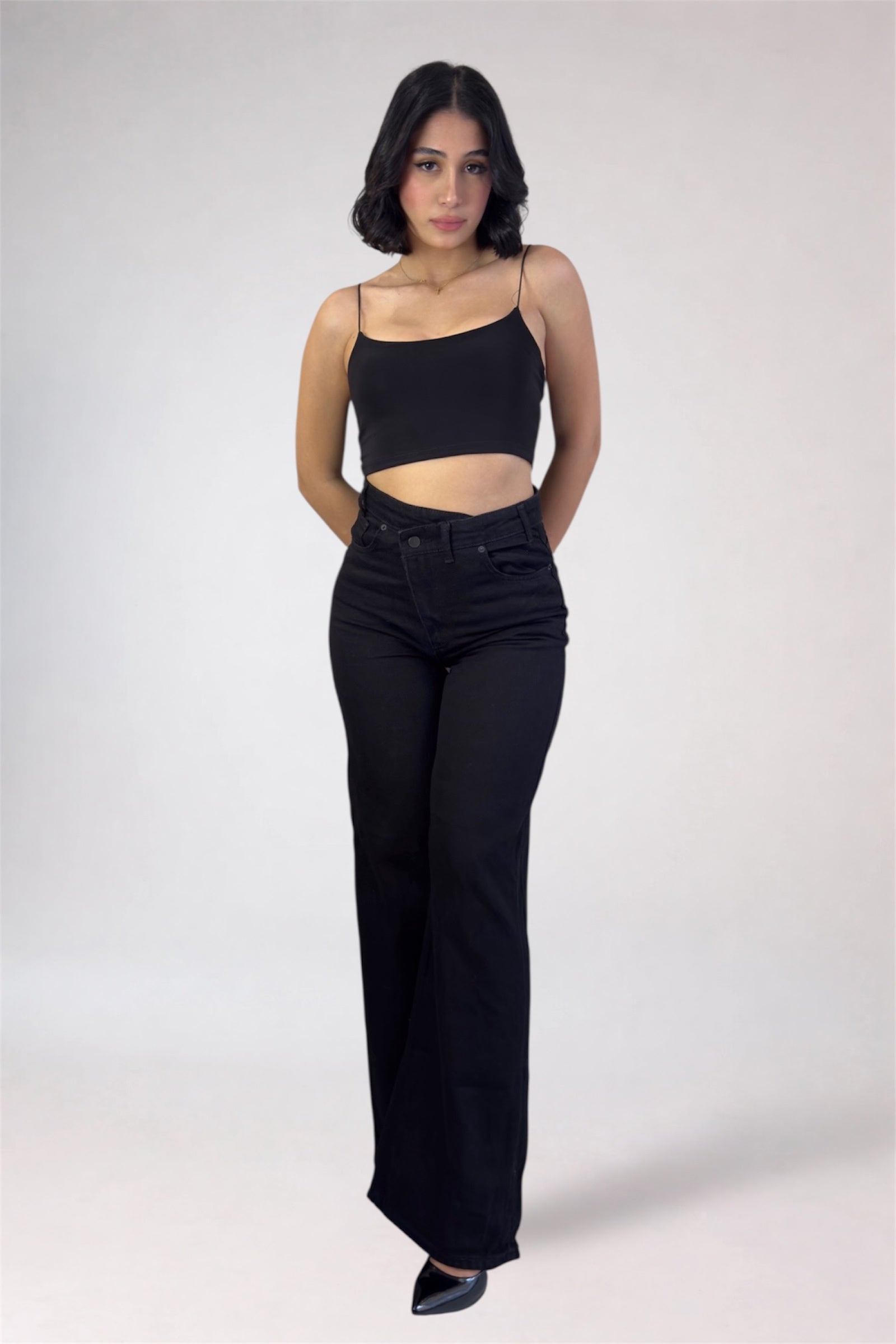 Woman wearing a black top and black high-waisted jeans on a white background