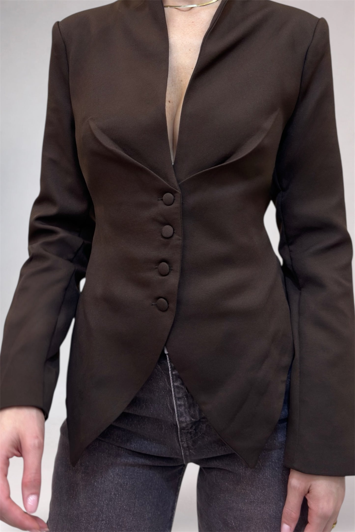 Brown blazer worn over a black top and jeans on a plain background