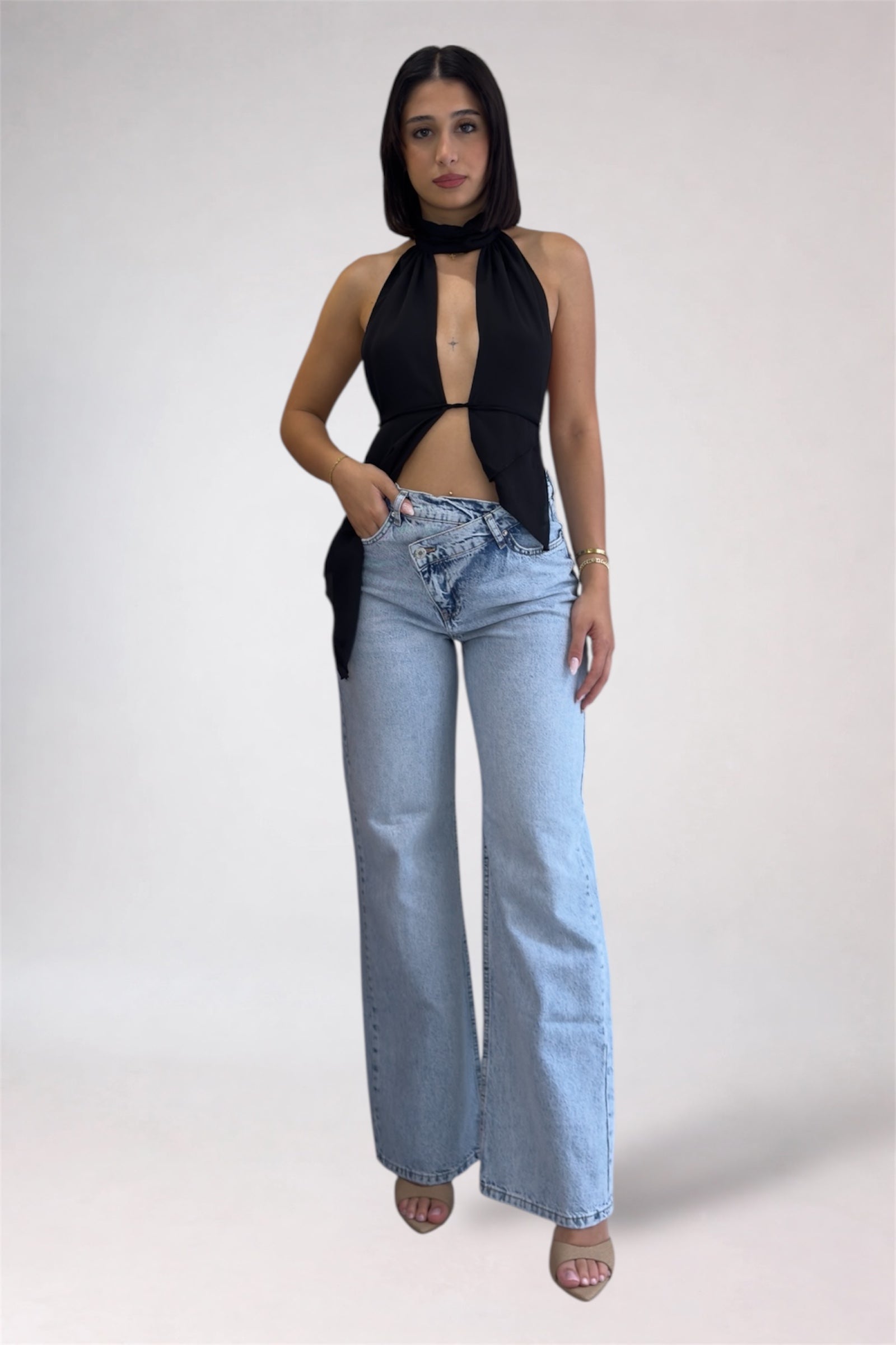 Woman wearing a black halter top and light blue jeans on a white background