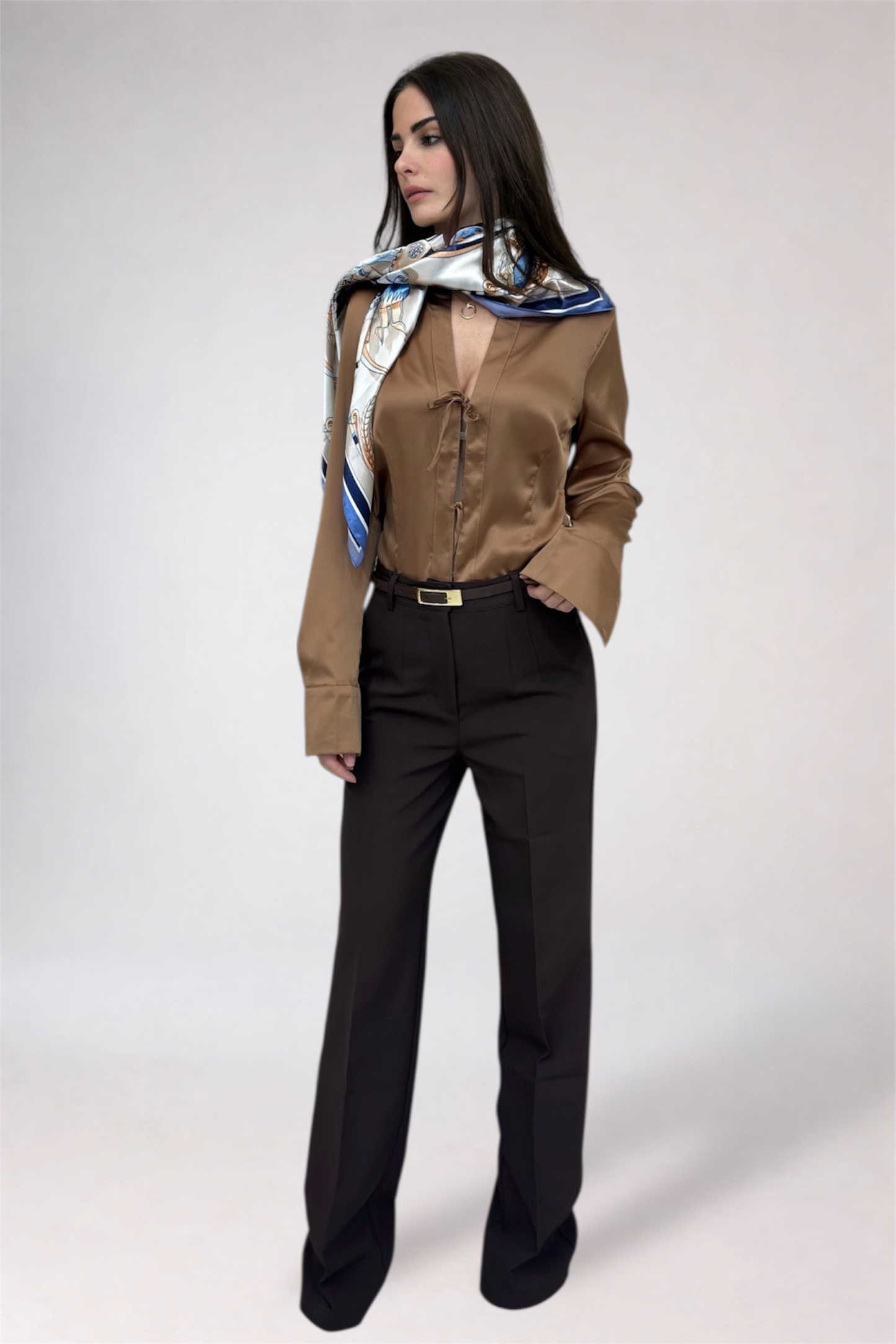 Woman wearing a brown shirt and black pants with a patterned scarf on a white background