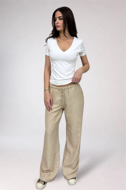 Woman wearing a white top and beige pants on a plain background