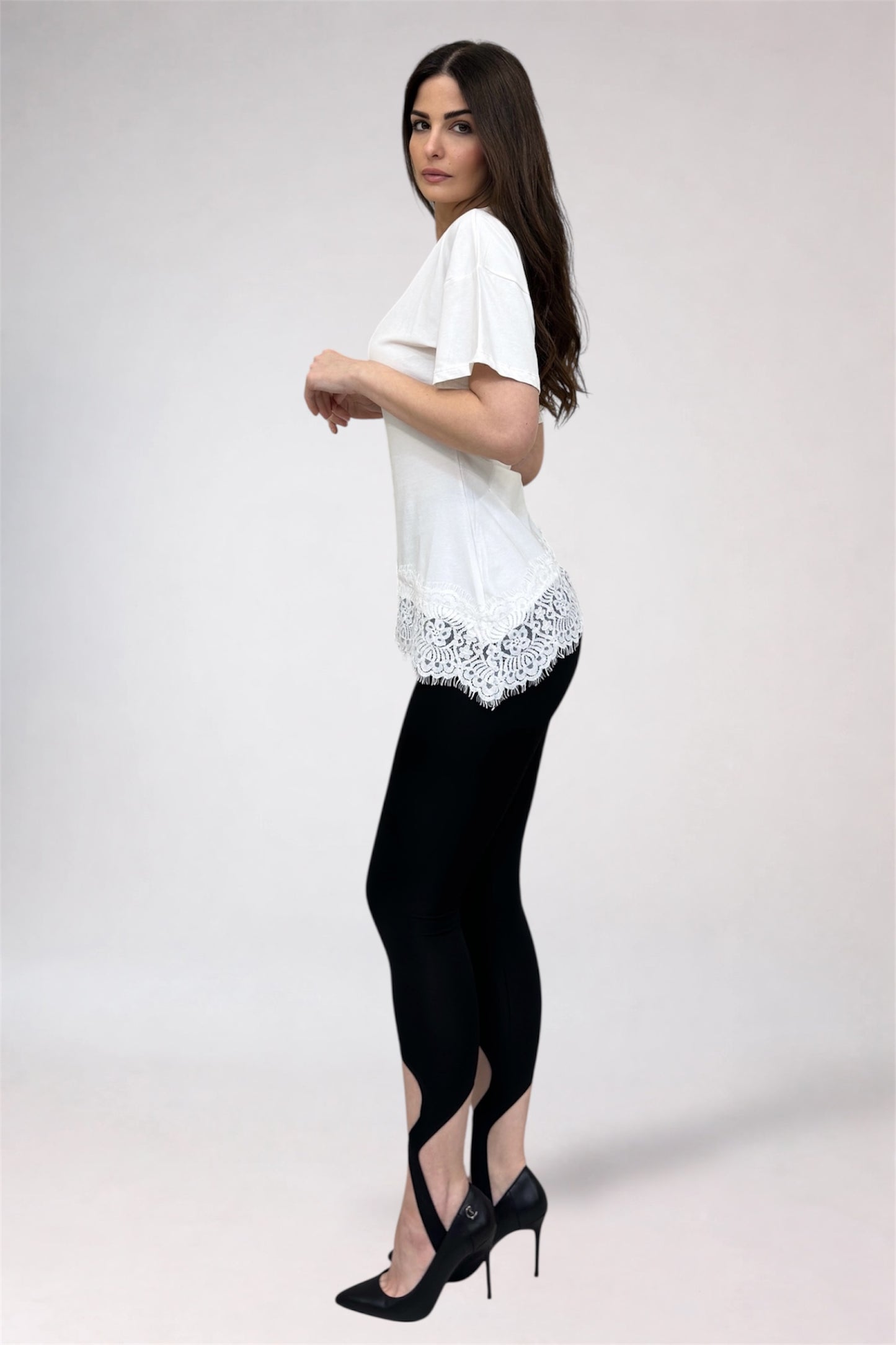 Woman wearing a white blouse with lace details and black pants on a plain background