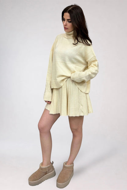 Woman wearing a light yellow sweater and skirt set with beige shoes on a white background