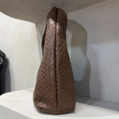 Brown woven handbag on a white surface with a neutral background