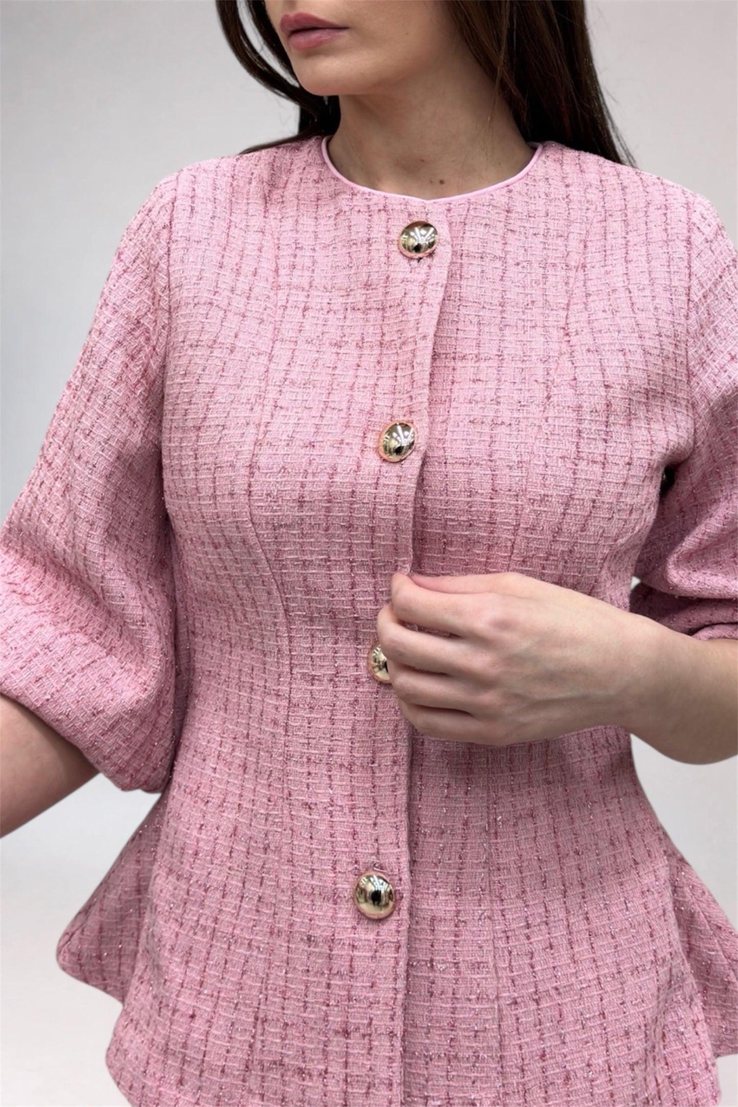 Close-up of a pink textured dress with buttons on a plain background