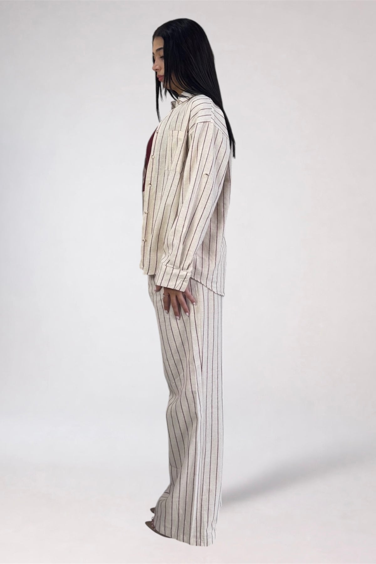 A model shown from the side profile wearing a matching two-piece pinstripe lounge set in cream and beige with thin dark vertical stripes, photographed against a plain light gray studio background.