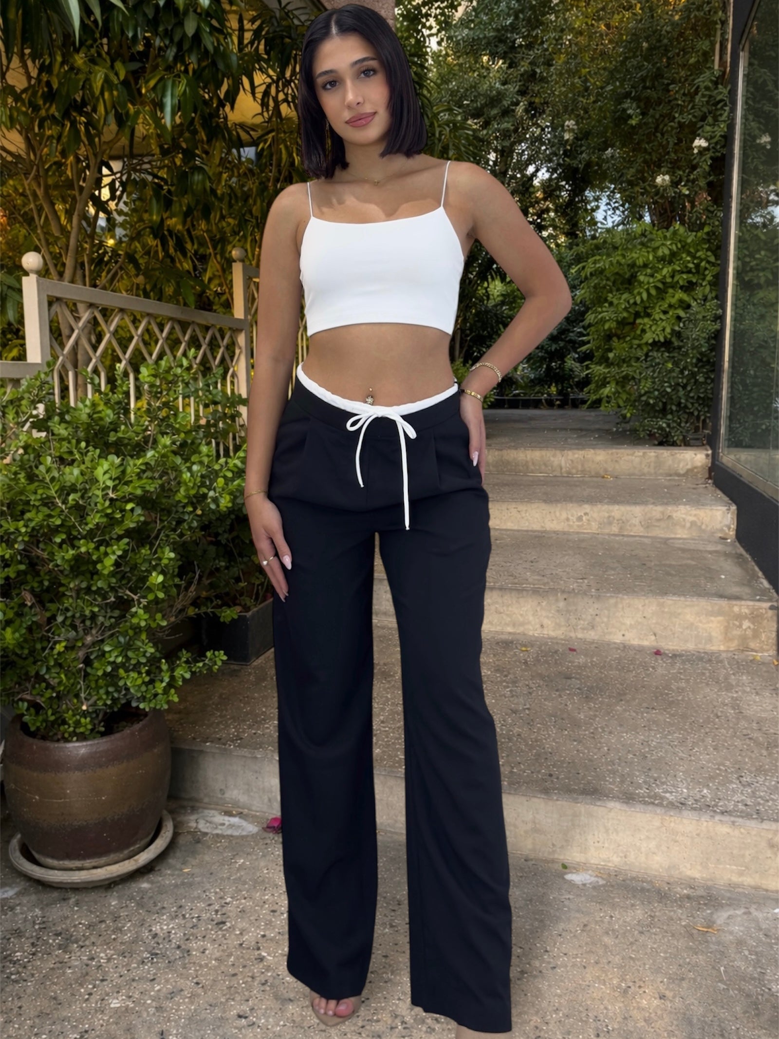 Woman wearing a white crop top and black pants standing outdoors on steps.