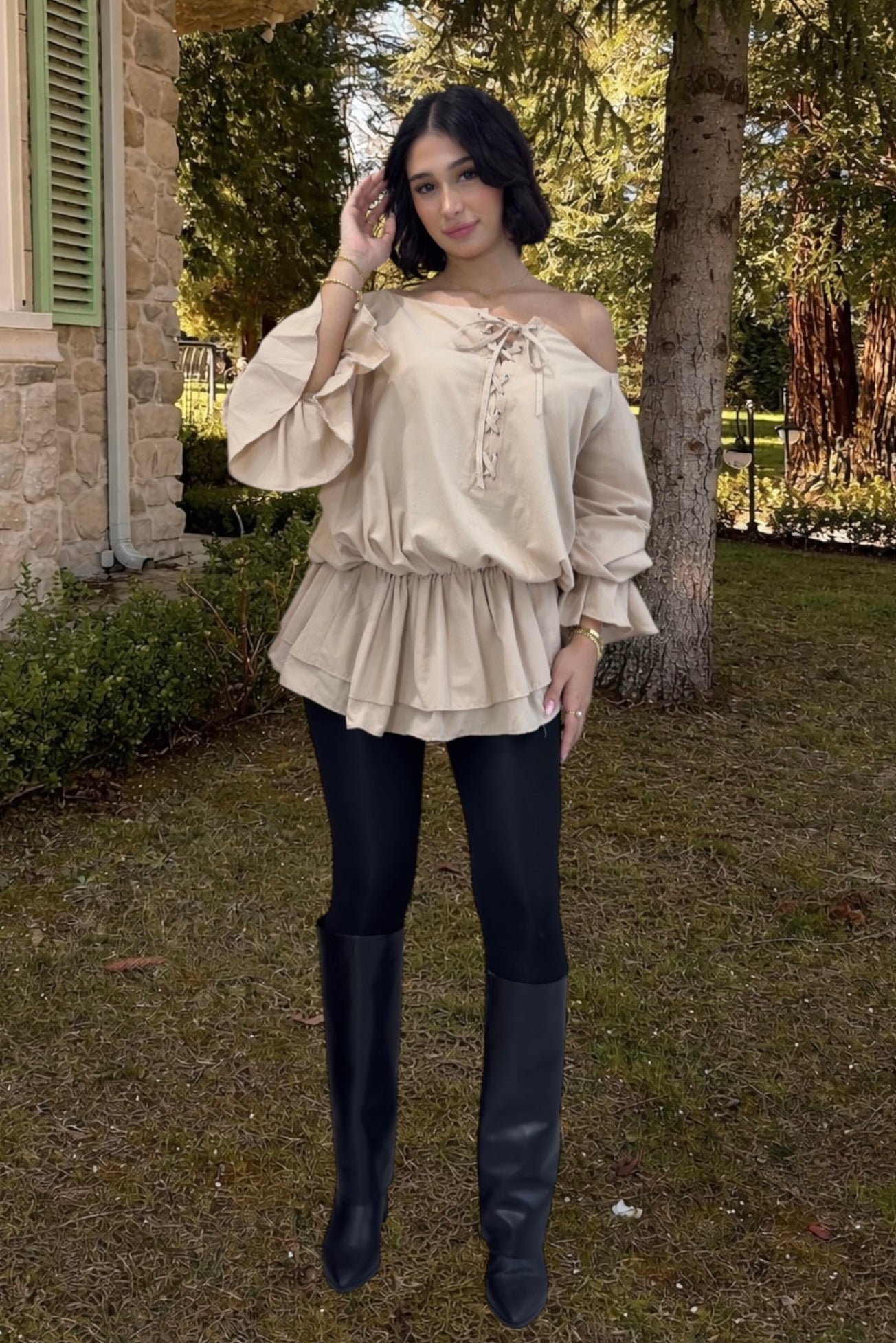 Woman wearing a beige off-shoulder blouse and black leggings outdoors.