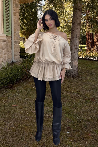 Woman wearing a beige off-shoulder blouse and black leggings outdoors.
